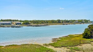 A coastal view with a pier extending into calm waters, surrounded by greenery and buildings in the background.