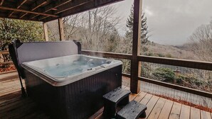 Uma banheira de hidromassagem em um deck de madeira, com vista para árvores e colinas.