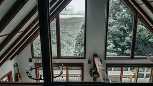Um quarto com teto inclinado, janelas amplas e vista para uma área arborizada.