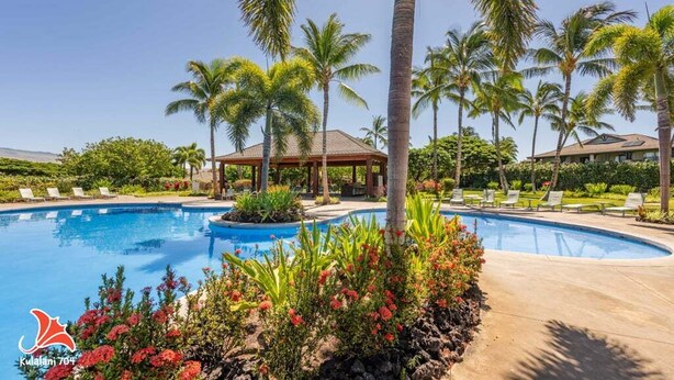 A swimming pool surrounded by palm trees and lounge chairs, with a gazebo and a building in the background. - Bright & quiet 2 bedroom in Kulalani, sleeps 6 (Kamuela)