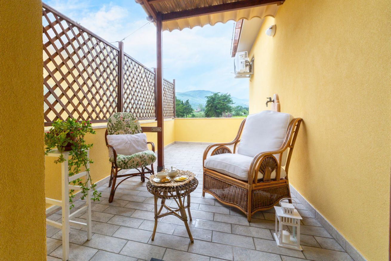 A balcony with wicker furniture, a small table with a teapot, and a lantern.