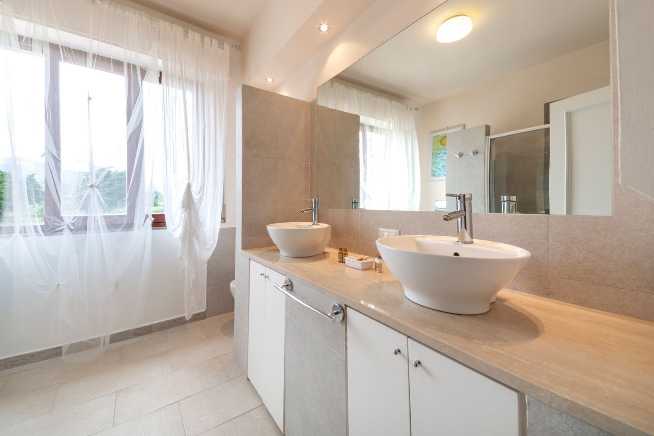 A modern bathroom with two sinks, a large mirror, and a view of the outdoors.