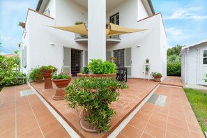 Un bâtiment blanc doté d’un patio carrelé, de plantes en pot et de mobilier d’extérieur.