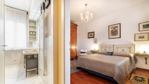 Un dormitorio con cama, mesita de noche, cómoda, candelabro y cuadros en la pared.