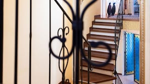Una escalera con barandilla de hierro forjado negro, escalones de madera y un portón azul en la parte inferior.