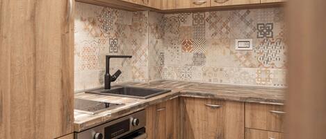 Una cocina con armarios de madera, un lavamanos de acero inoxidable y azulejos decorativos en la pared.