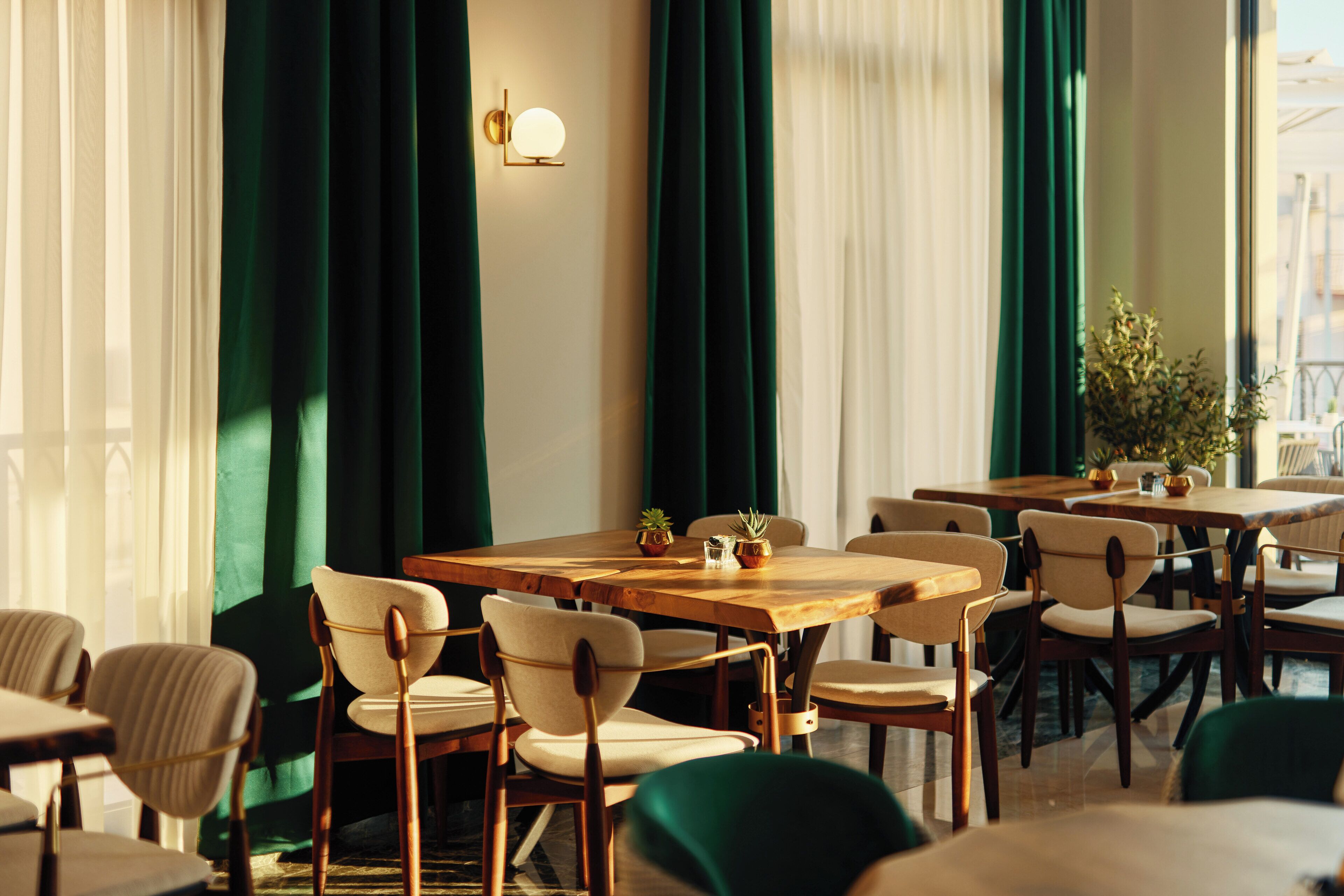 A restaurant with wooden tables and chairs, green curtains, and a wall-mounted light fixture.