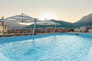 A swimming pool with umbrellas, surrounded by buildings and mountains in the background. - Hotel Diplomat (Budva)