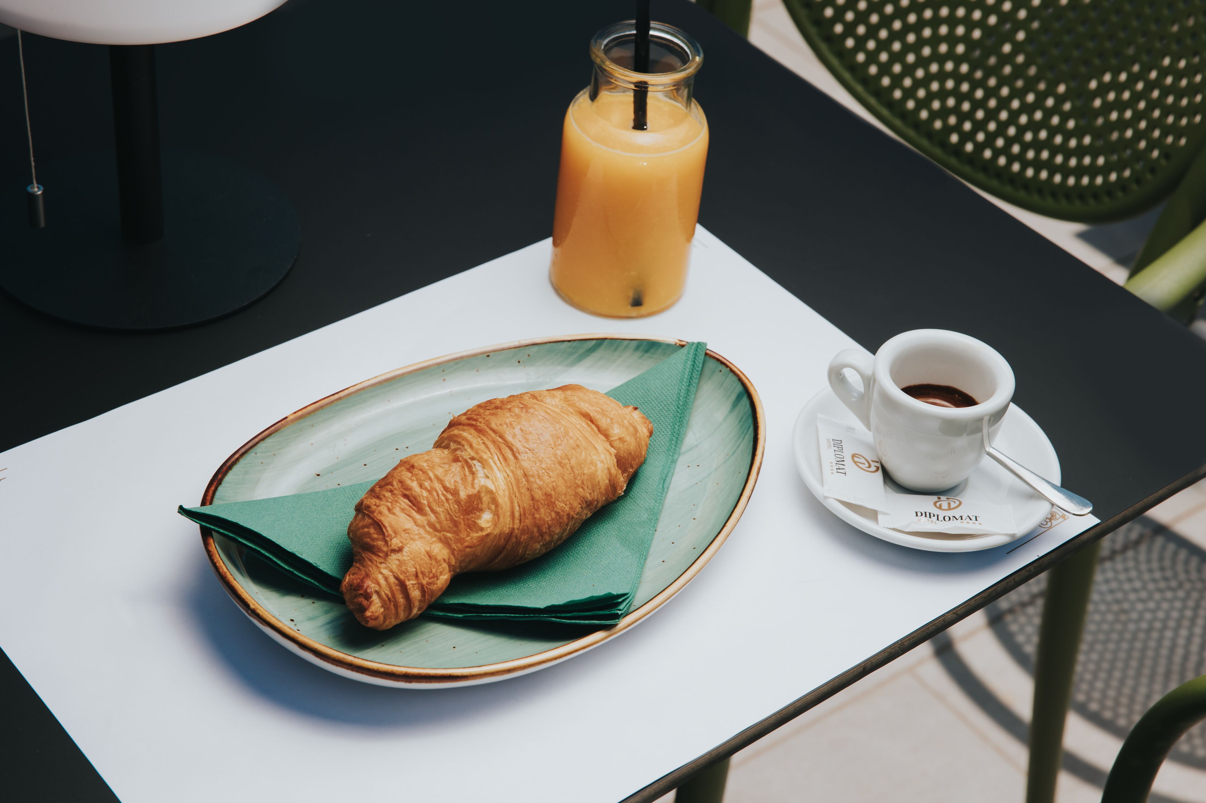 A table with a croissant on a plate, a glass of orange juice, and a cup of coffee.