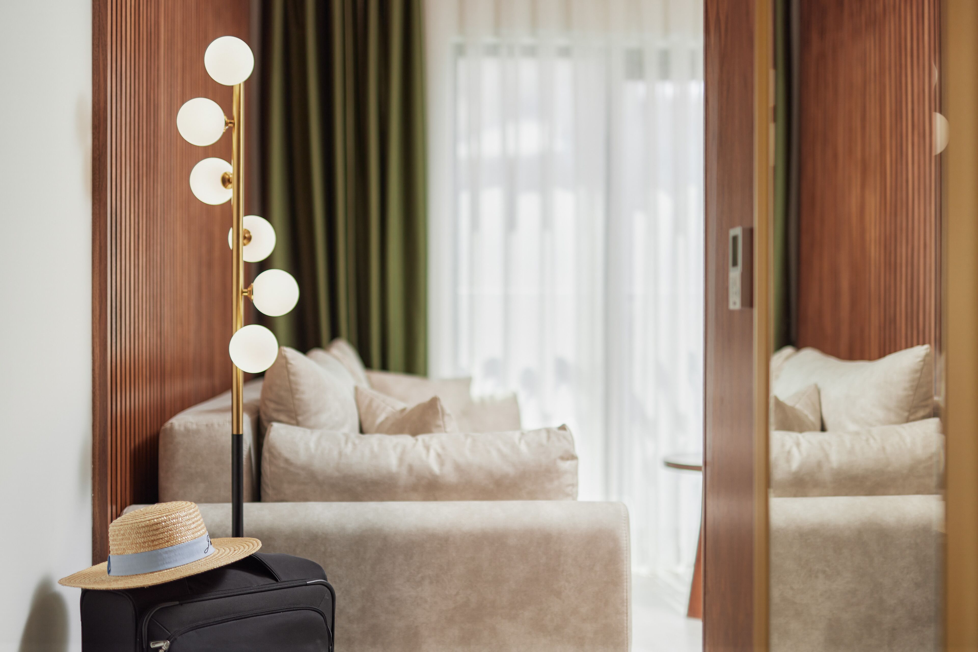 Hotellihuone, jossa on sänky, matkalaukku, hattu ja lamppu, jossa on valot.