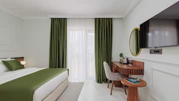 Una habitación de hotel con cama, escritorio, silla, televisión y ventana con cortinas.