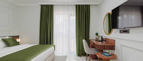 Una habitación de hotel con cama, escritorio, silla, televisión y ventana con cortinas.