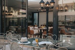 An outdoor cafe with glass tables and chairs, a street lamp, and a view of the interior dining area. - Hotel Diplomat (Budva)