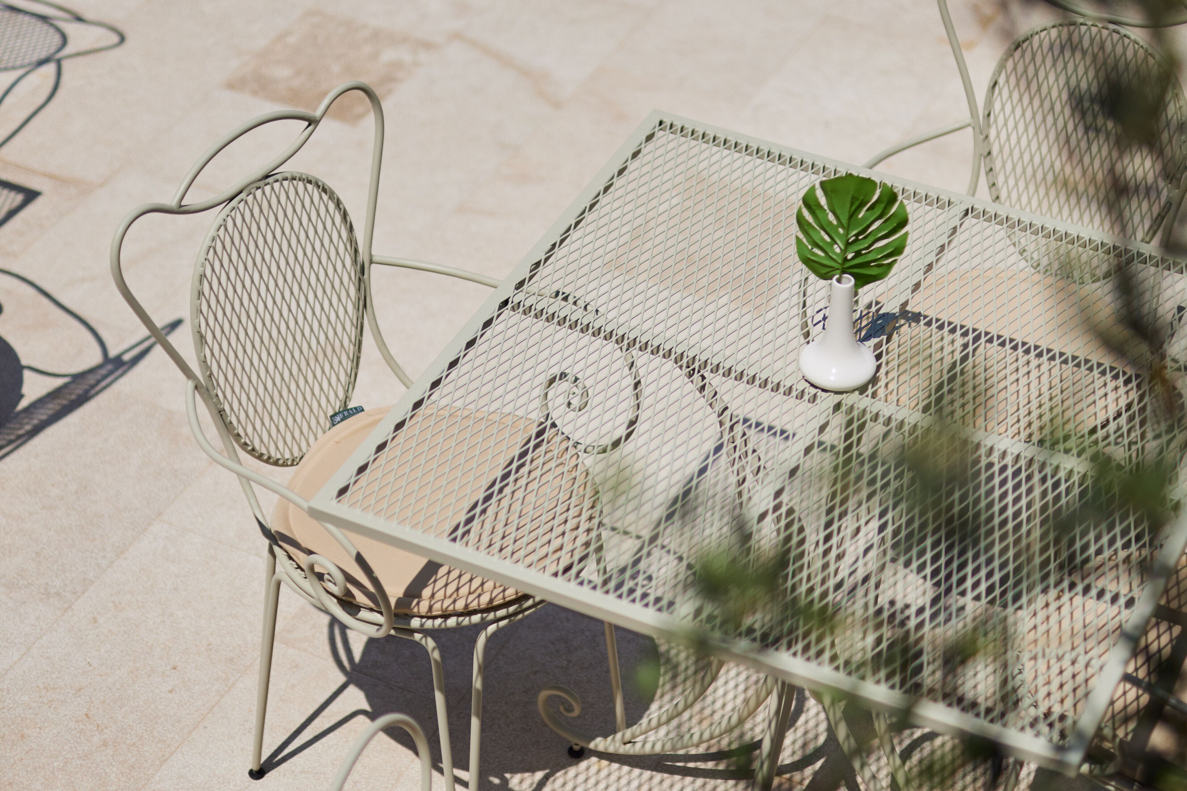 A metal table with a woven seat and a white vase with a green leaf.
