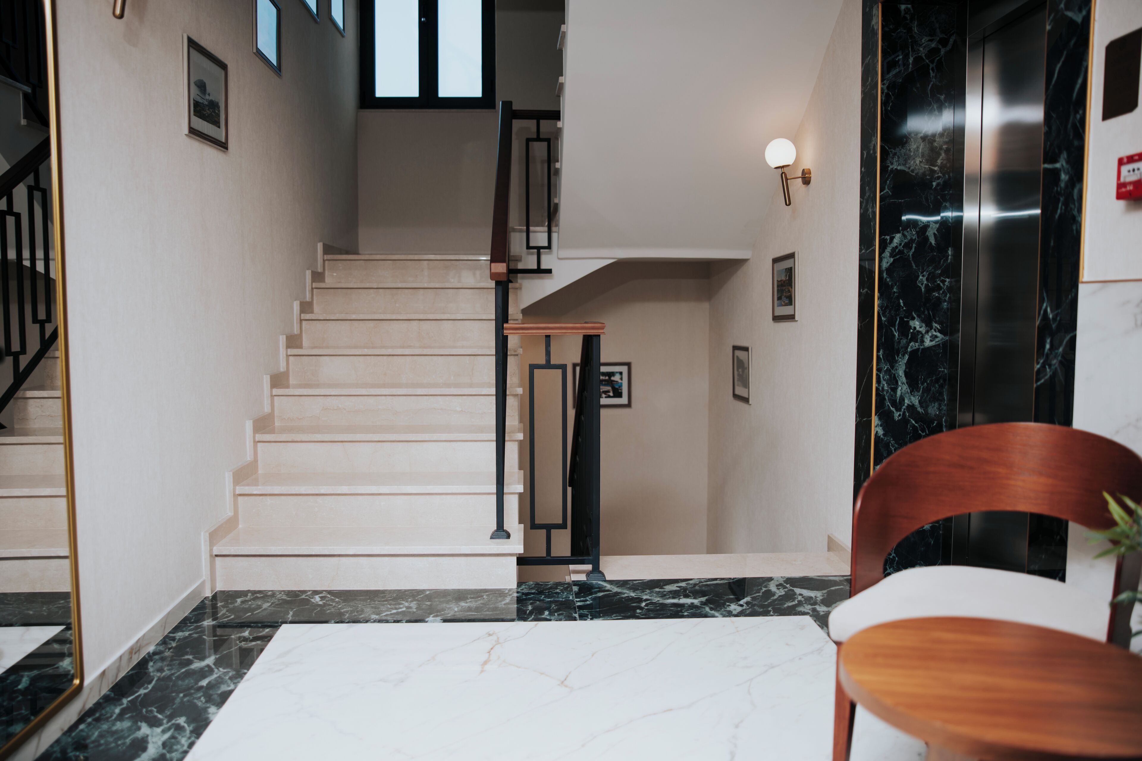 Un interior moderno con una escalera, suelo de mármol y una silla de madera.