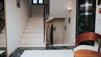 Un interior moderno con una escalera, suelo de mármol y una silla de madera.