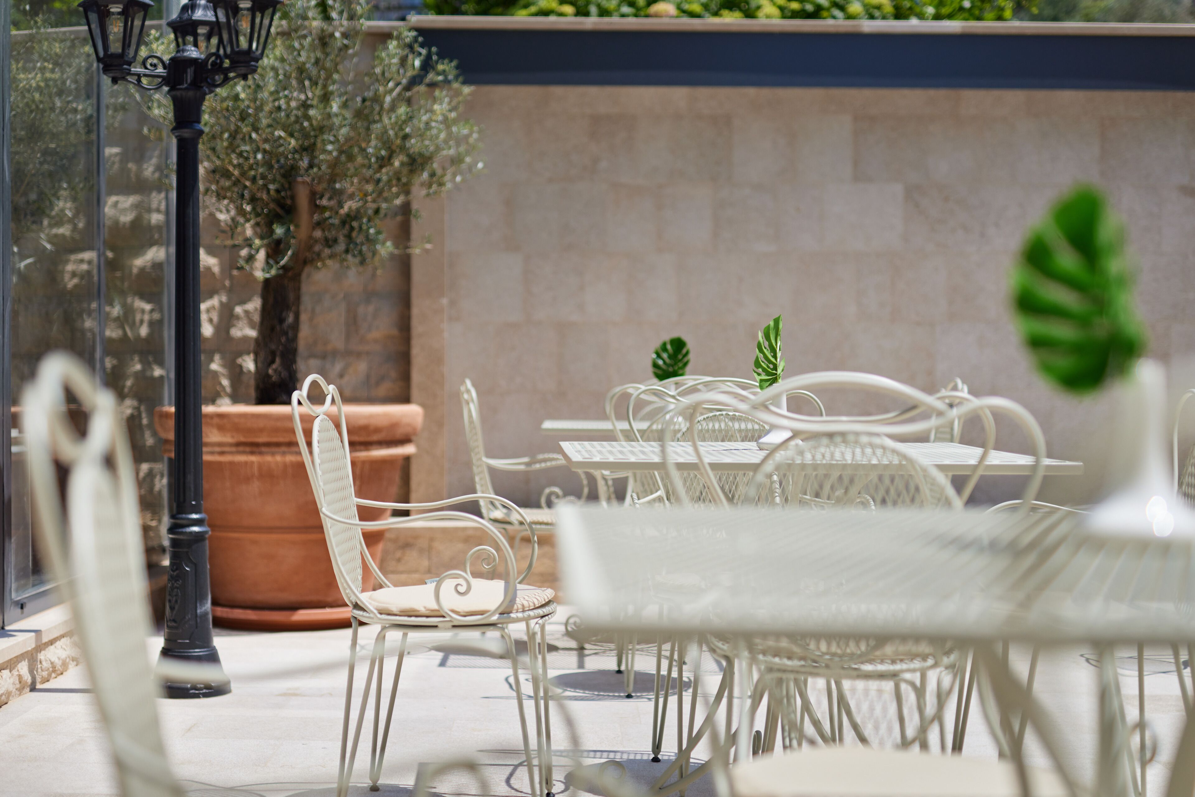 Un patio con sillas y mesas de metal blanco, una planta en maceta y una farola.