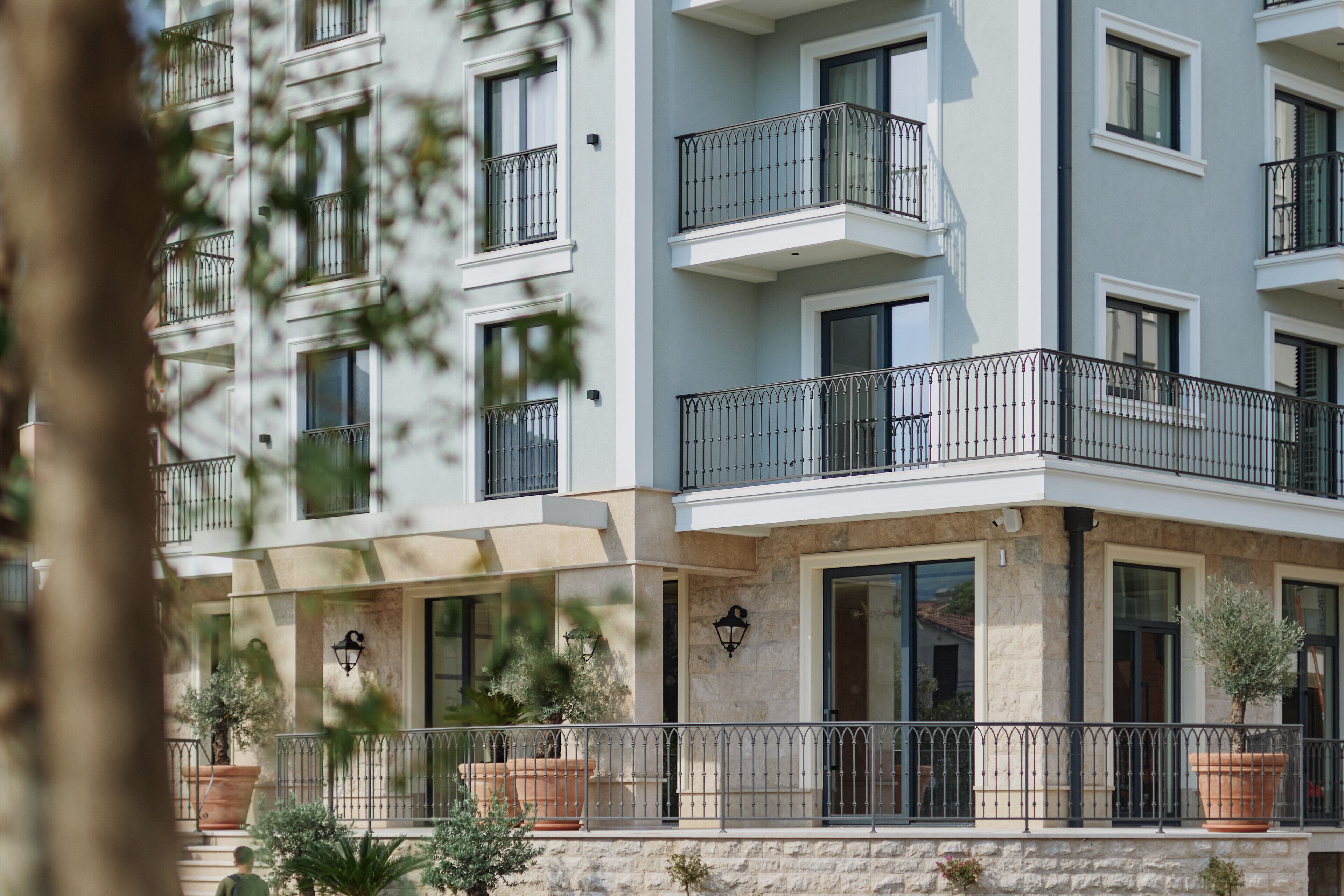 A multi-story residential building with balconies, large windows, and potted plants.