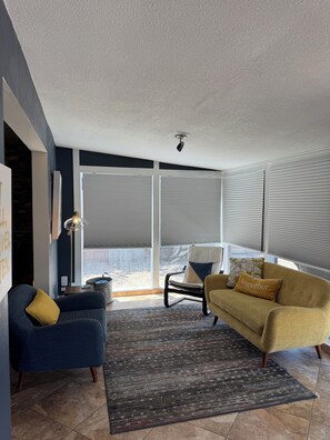 A modern living room with a sofa, armchair, and a large window with blinds. - 4BR 3 BA Family Retreat, Real AC, 15 Min to Downtown, Pet Friendly (Albuquerque)