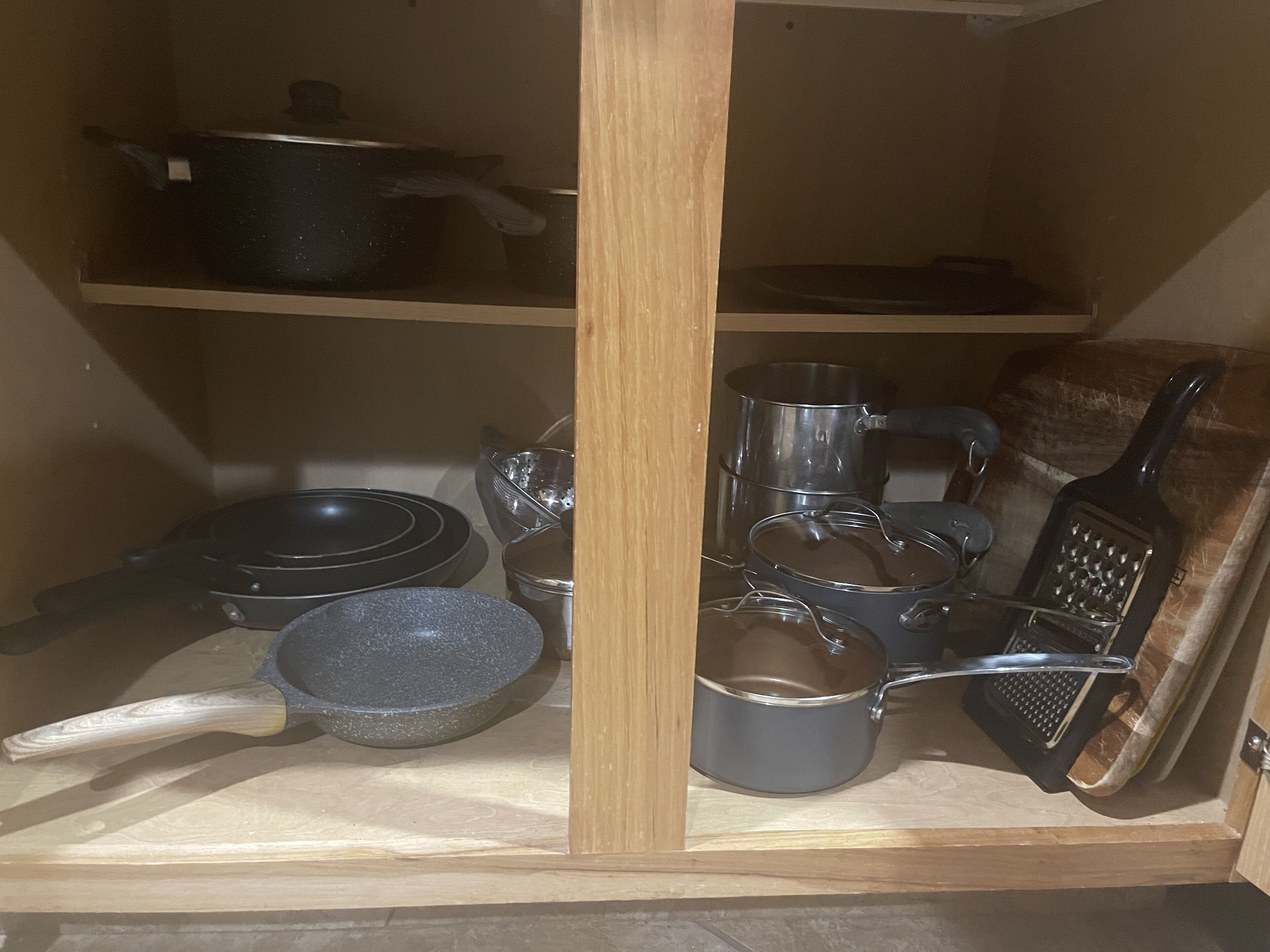 Un pensile da cucina con diversi utensili, tra cui pentole, padelle e una grattugia.