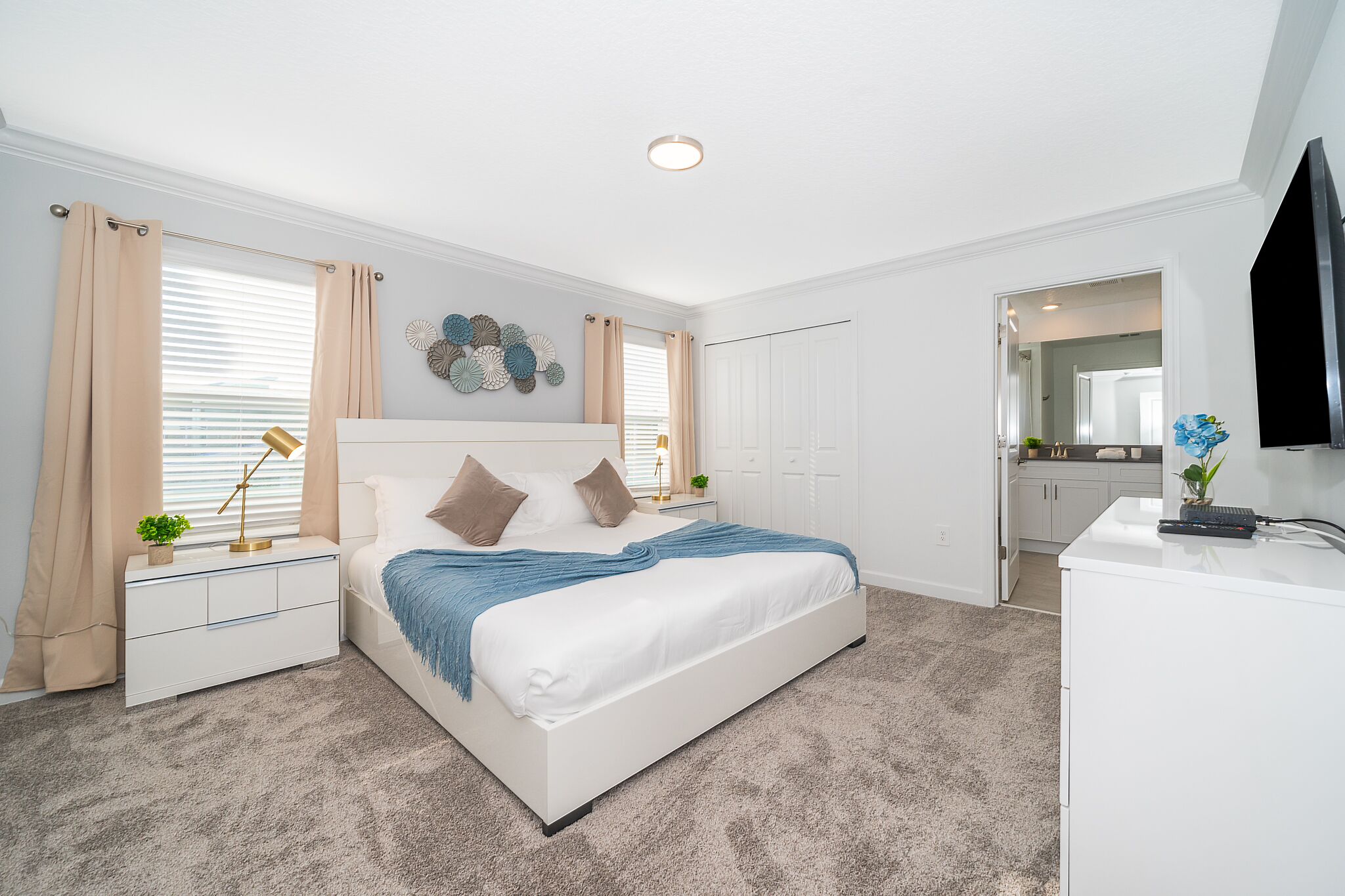 A modern bedroom with a large bed, bedside tables, a desk, and a television.