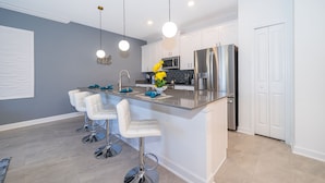 Una cocina moderna con armarios blancos, electrodomésticos de acero inoxidable y una isla central con taburetes de bar.