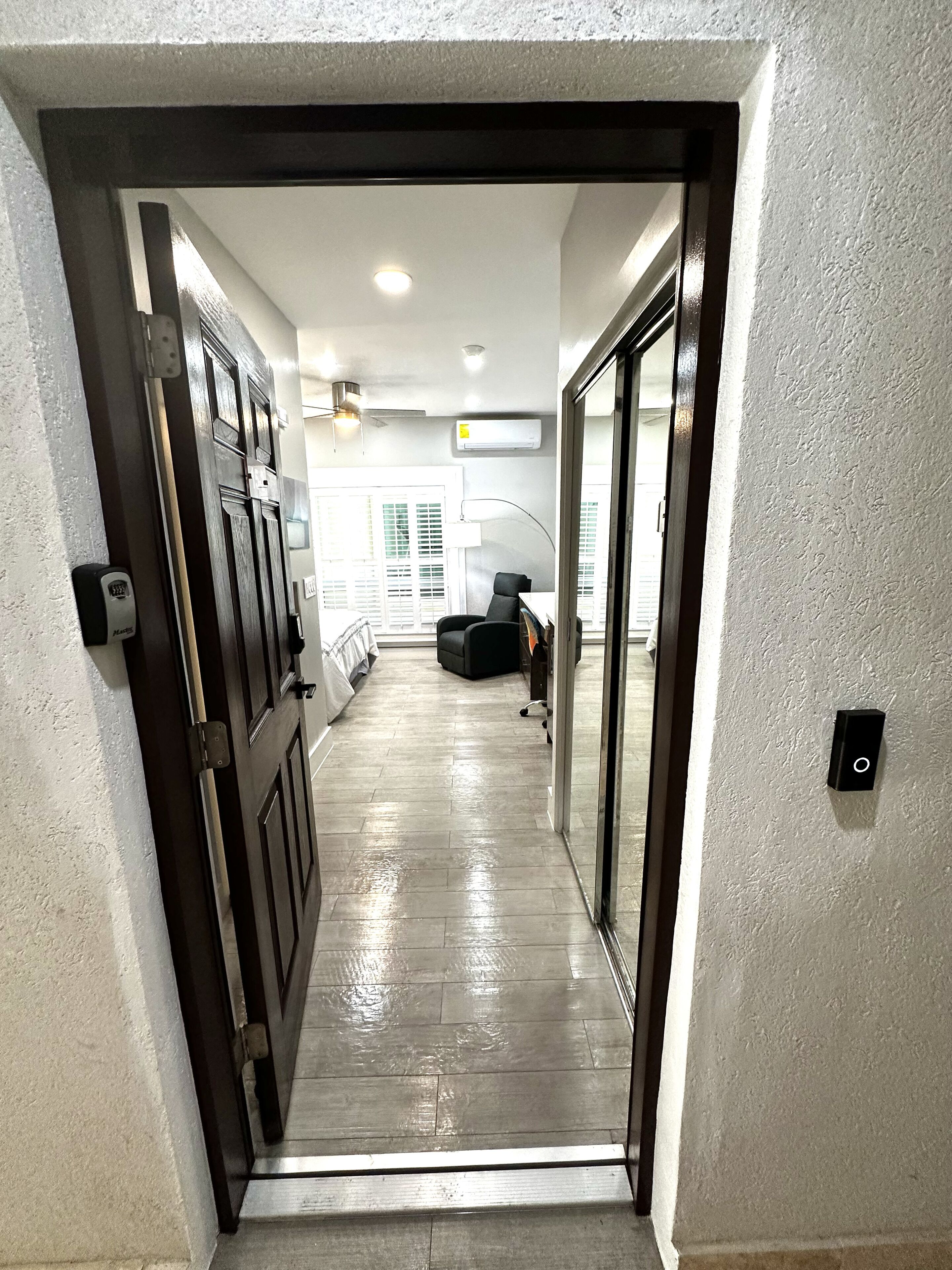 A hallway with a wooden floor, a door with a black handle, and a white wall with a textured finish.