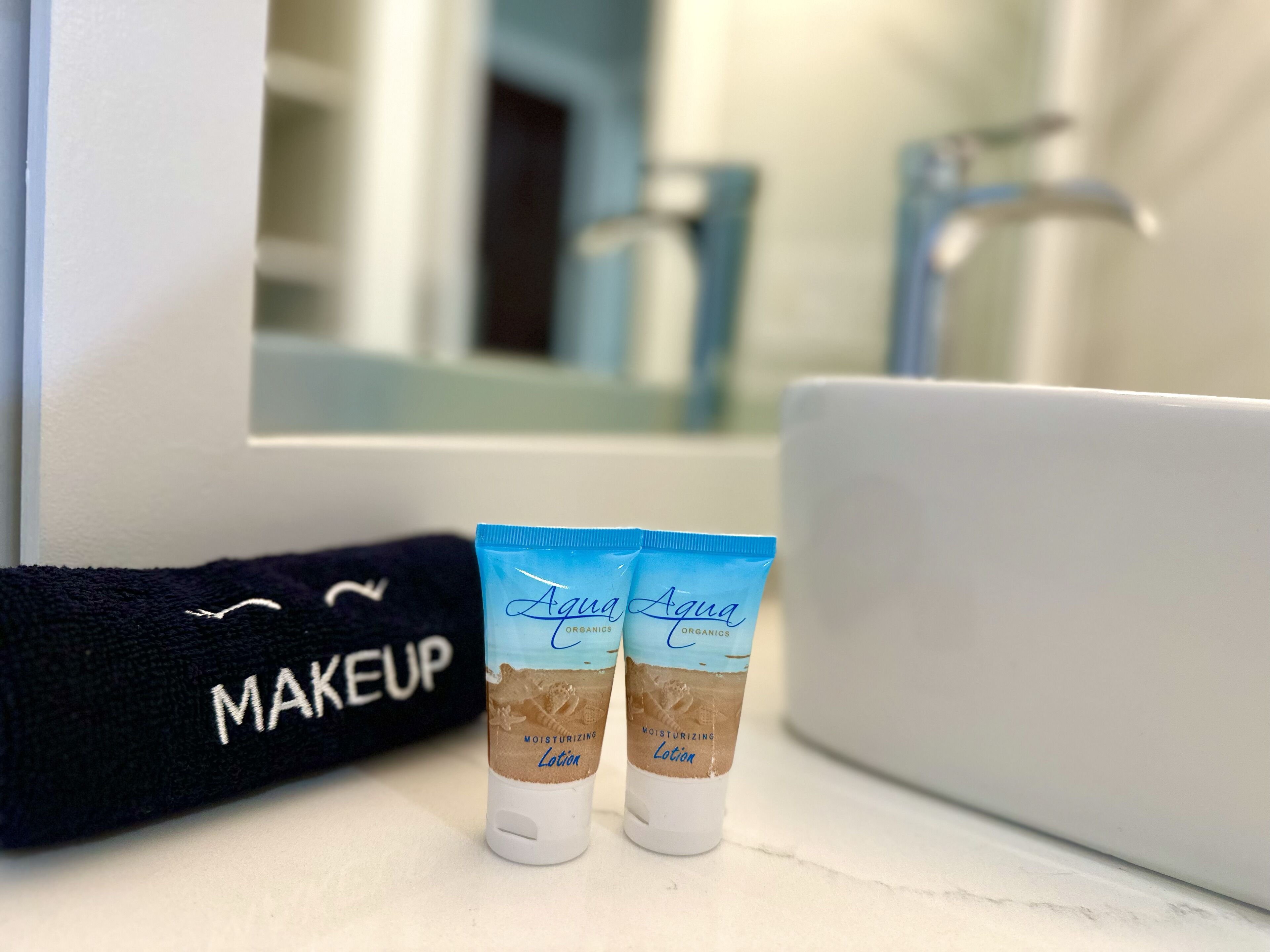 En sminkväska med texten ”MAKEUP” och två tuber med ”Aqua Organics Återfuktande Lotion” placerade framför en spegel.