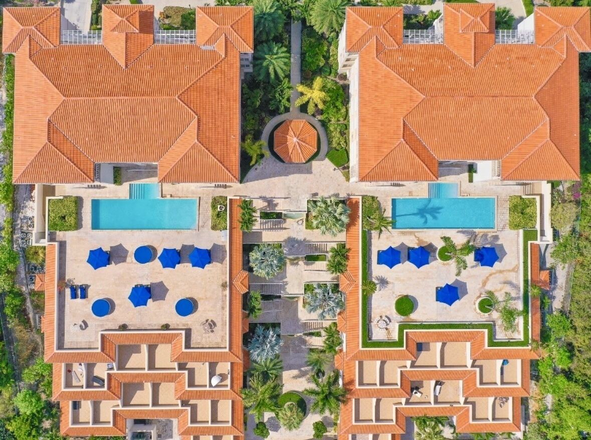 Vista aérea de un complejo turístico con dos piscinas, zonas de descanso y un patio central.