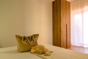 A room with a bed, a large beige bag, and a straw hat on a woven mat.