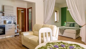 A compact room with a kitchenette, a sofa, a dining table, and a bed with curtains. - Morgana House-Beachfront (Roccalumera)