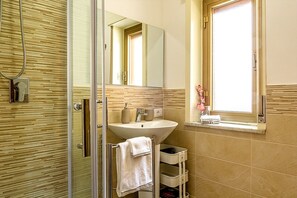 A bathroom with a glass shower enclosure, a sink with a mirror above it, and a window with a view.
