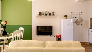 A modern living room with a flat-screen TV, a sofa, a dining table with chairs, and a kitchen area with a refrigerator and a grid-patterned wall decoration. - Morgana House-Beachfront (Roccalumera)