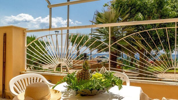 A table with a white tablecloth, a white chair, and a decorative bowl with fruits and greenery. - Morgana House-Beachfront (Roccalumera)