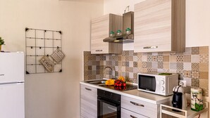 A compact kitchen with a microwave, oven, and sink. There are wooden cabinets and a grid wall decoration. - Morgana House-Beachfront (Roccalumera)
