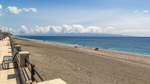 A beach with a paved walkway, benches, and a railing. - Morgana House-Beachfront (Roccalumera)