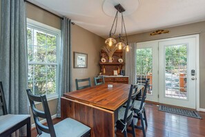 A dining area with a wooden table, chairs, a chandelier, and a view through a glass door.