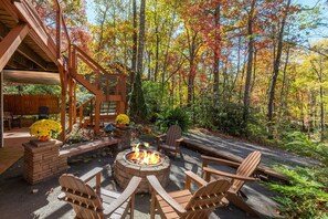 An outdoor patio with a fire pit, wooden chairs, and a stone fireplace. - Abundant Peace | Montreat Home with Fire Pit, Gas Grill & Mountain Views! (Montreat)