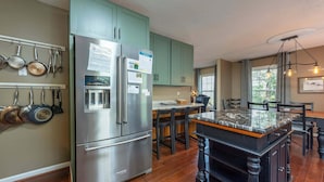 Una cocina con refrigerador de acero inoxidable, armarios verdes, una isla de mármol y una zona de comedor con sillas.