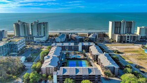 Un complejo hotelero de gran altura con varios edificios, un patio central con cancha de tenis y vista al océano.