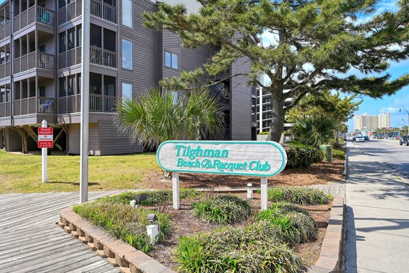 Une enseigne indiquant « Tilghman Beach & Racquet Club », avec une promenade en bois menant à un bâtiment doté de balcons.