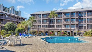 Un hotel con piscina, sillas de descanso y un patio cubierto.