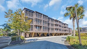 Un edificio de varios pisos con balcones, estacionamiento y una palmera.
