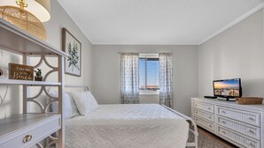 Un dormitorio con cama, cómoda, televisor y ventana con cortinas.