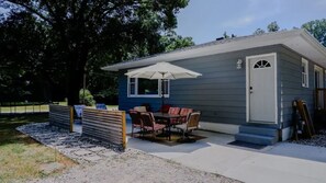 A small house with a patio, a dining table with chairs, and a white umbrella.