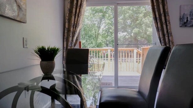 Una stanza con un tavolo in vetro, una sedia, una pianta in vaso e vista su una terrazza e alberi.