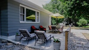 A covered patio with outdoor furniture, a table, and chairs, surrounded by a wooden fence and potted plants.
