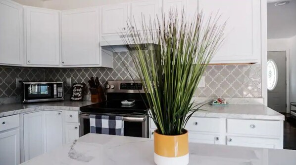 A modern kitchen with white cabinets, a microwave, a stove, and a potted plant.