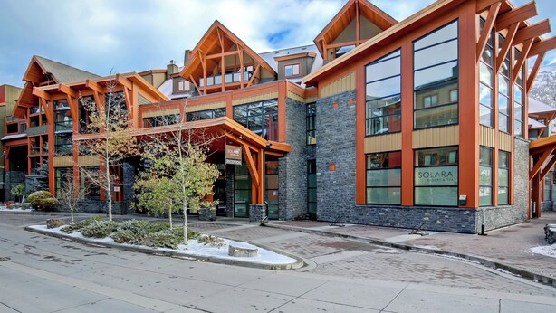 A modern building with large windows and a stone facade, labeled "Solara Resort & Spa". - Bow 119 | Adorable Suite with Pool & Hot Tub (Canmore)