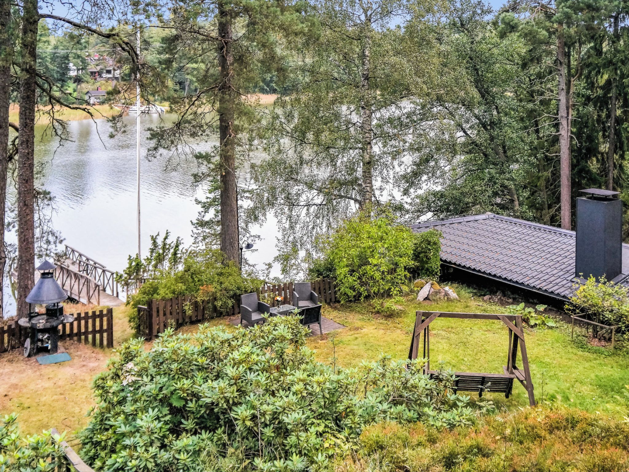 A lakeside property with a deck, outdoor seating, and a wooden play structure.